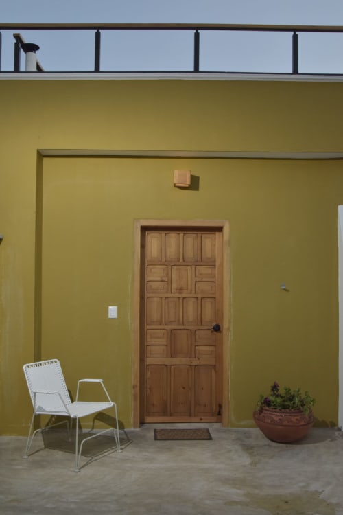 Fachada amarillo brillante de Casa Cafeólogo con puerta de madera, silla blanca y planta macetada en San Cristóbal