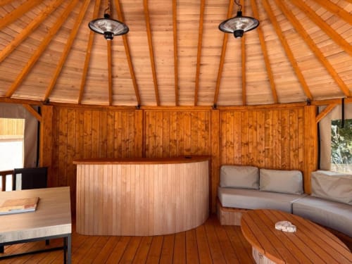 Intérieur de villa en bois avec plafond conique, chauffages de terrasse, comptoir de bar incurvé et sièges gris aux Villas d'A Storia,