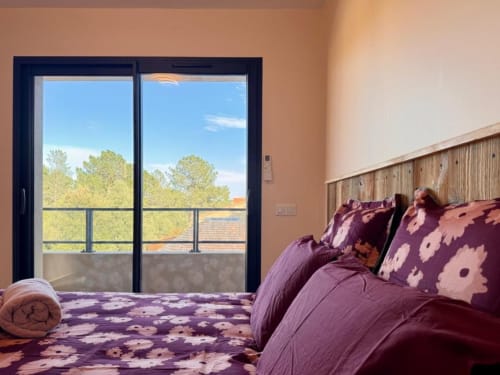 Chambre aux draps floraux violets aux Villas d'A Storia à Porto-Vecchio, avec balcon donnant sur les arbres et ciel dégagé