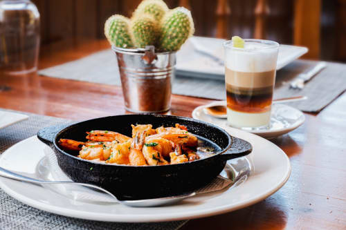 Camarones salteados en sartén de hierro en el restaurante hostal Casona del Porma, con planta de cactus y bebida de café en capas.