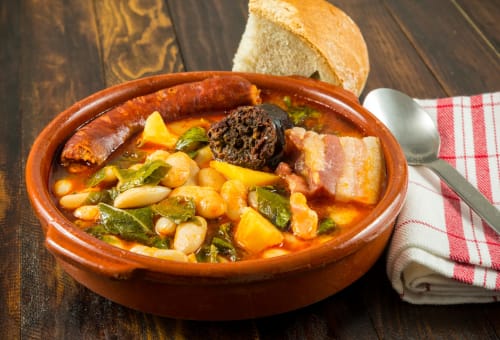 Tradicional estofado español con alubias, carnes y verduras servido en cuenco de cerámica en la Casona del Porma