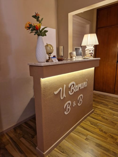 Banco reception di U Baruni B&B a Messina con vaso bianco, lampada e specchio
