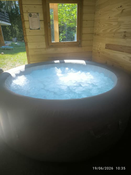Bain à remous fumant dans une cabane en bois aux Insolites de la Bastide, avec vue sur le jardin verdoyant