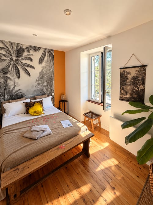 Chambre tropicale à la Maison Farol B&B avec tête de lit en feuilles de palmier, oreiller jaune, parquet et vue sur la ville de Salles.