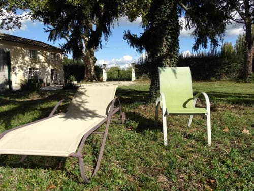 Jardin ensoleillé des gîtes de Val à Cabannes avec transats et chaises sous de grands arbres matures