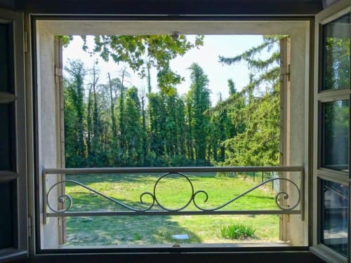 Fenêtre ouverte avec balustrade ornementale donnant sur un jardin paysagé et des paysages forestiers aux gîtes de Val, Cabannes