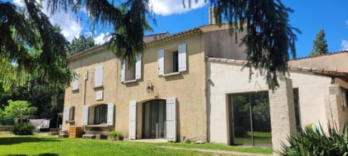 Bâtisse principale aux Gîtes de Val, maison de pierre provençale avec volets blancs, jardin fleuri et pelouse verdoyante en Provence