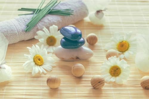 Ambiance spa et bien-être avec pierres empilées, marguerites et perles en bois sur natte de bambou aux gîtes de Val