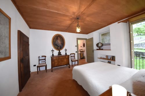 Camera elegante a Roseto del Drago con soffitto in legno, mobili antichi, letto bianco e vista giardino dalla porta-finestra