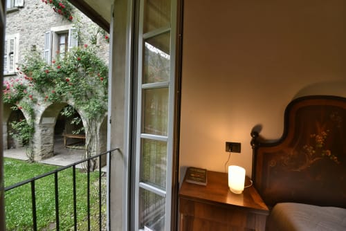 Camera da letto di Roseto del Drago con vista giardino attraverso le porte in vetro, arredamento in legno e illuminazione calda