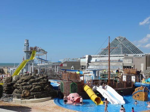 Parc aquatique coloré avec toboggans, navire pirate et vue sur l'océan dans une station balnéaire française