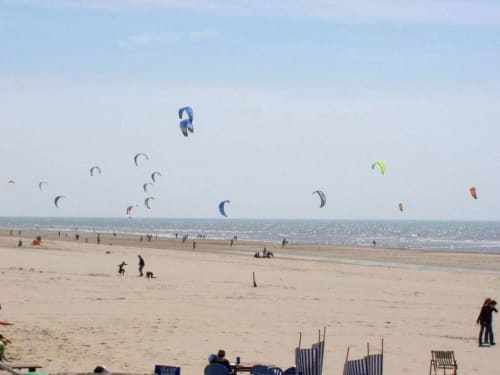 Plusieurs cerfs-volants colorés survolant une plage de sable à Beussent, France avec des baigneurs et des chaises longues rayées