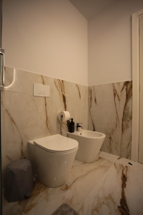 Bagno moderno in Totonno's Rooms, Tropea con piastrelle effetto marmo, sanitari bianchi e design contemporaneo