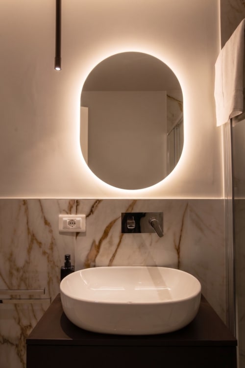 Bagno moderno con specchio ovale illuminato, lavabo bianco a bacinella e pareti in marmo presso Totonno's Rooms a Tropea