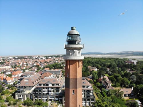Phare historique en brique rouge dominant la ville de Beussent avec ses bâtiments résidentiels et paysage campagnard