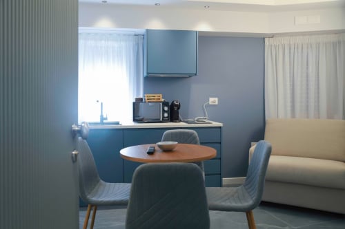 Moderna camera d'hotel Totonno's Rooms a Tropea con angolo cottura blu, tavolo da pranzo e divano color crema