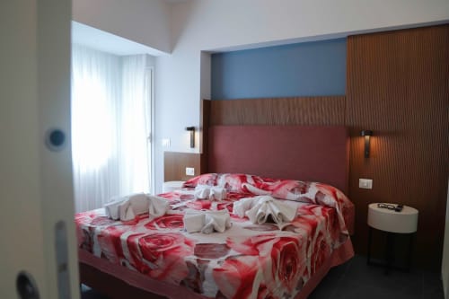 Camera moderna alle Totonno's Rooms di Tropea con biancheria rossa, rivestimenti in legno e vista sulla città dal balcone.