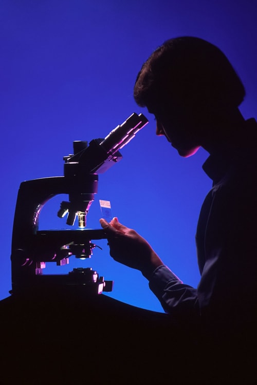 Silhouette d'un scientifique utilisant un microscope sur fond bleu à la Auberge Yasi Lyon