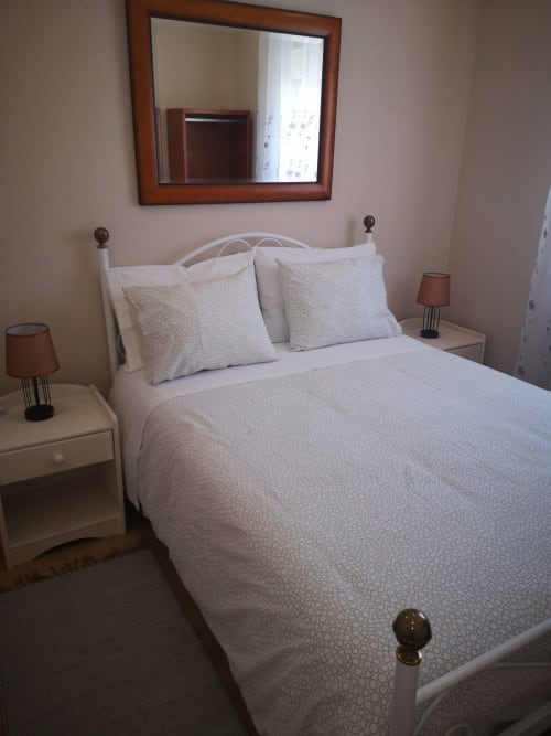 Quarto luminoso na villa Feather House Adega em São Bartolomeu com roupa de cama branca, espelho com moldura de madeira e mesinha de cabeceira