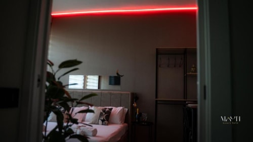 Lussuosa camera matrimoniale presso Moon Rooms By Celeste a Catania con illuminazione neon rossa, biancheria rosa e vista sulla città