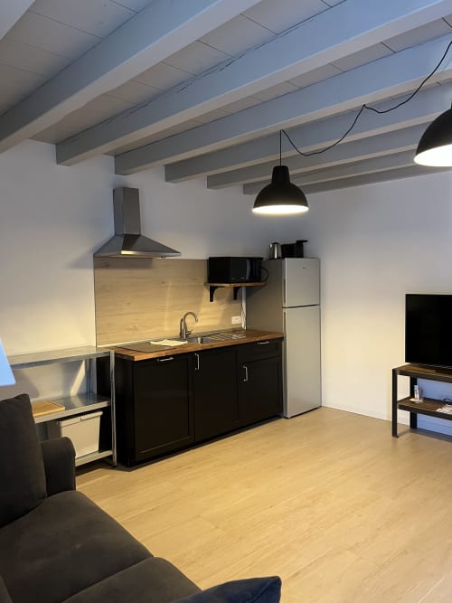 Cucina-soggiorno moderna in appartamento a Bergamo con armadi neri, frigorifero in acciaio inossidabile, travi a vista