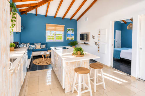 Cuisine et séjour de l'appartement Aigue-marine au Quetzal à Sainte-Anne avec murs bleus, poutres en bois et vue sur la piscine