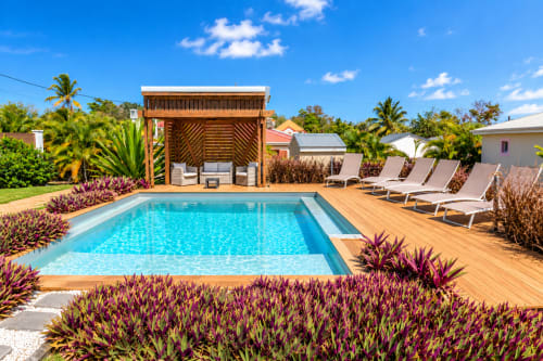 Appartement Le Quetzal avec vue sur la piscine à Sainte-Anne, Guadeloupe : transats, terrasse en bois et jardins tropicaux