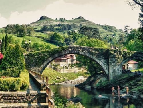 Puente de piedra histórico sobre el río en el hotel La Calleja Real de Liérganes, España, rodeado de exuberantes laderas verdes