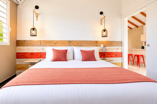 Chambre moderne au Quetzal avec tête de lit en bois rayé, accents rouges, luminaires suspendus et literie blanche à Sainte-Anne