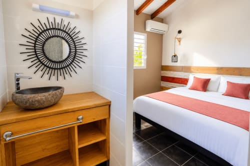 Salle de bain et chambre de l'appartement Kâz corail au Quetzal, Sainte-Anne avec miroir soleil et literie corail