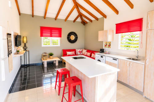 Cuisine moderne Kâz corail avec accents rouges, îlot de cuisine et vue piscine au Quetzal, Sainte-Anne