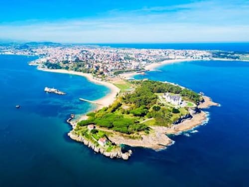 Vista aérea de pueblo costero con playas y península boscosa en aguas azules del Mediterráneo