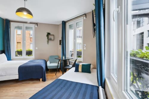 Modern studio apartment at Résidence Aurmat Paris with two beds, seating area, kitchenette, and balcony views in