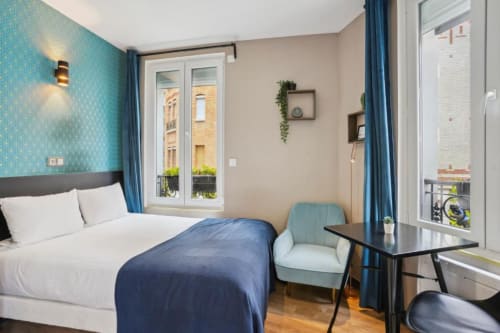 Modern studio bedroom at Résidence Aurmat Paris Boulogne with turquoise wallpaper, double bed, blue armchair, desk, and