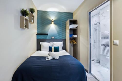 Modern Superior Double Studio bedroom at Résidence Aurmat Paris Boulogne with navy bed, teal wallpaper, wooden shelving, and