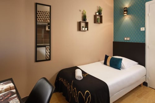Chambre moderne à la Résidence Aurmat Paris avec lit, miroir, plantes murales, mur d'accent bleu canard et parquet.
