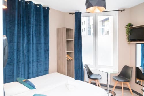 Studio bedroom at Résidence Aurmat Paris with twin bed, blue curtains, desk, and balcony view overlooking