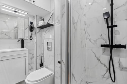 Modern bathroom with marble walls, white sink, toilet, and black rainfall showerhead at Résidence Aurmat Paris Boulogne.