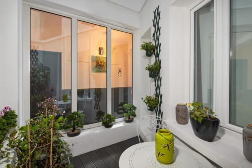 Modern balcony at Résidence Aurmat Paris with potted plants, window views into bright studio apartment, and white furniture