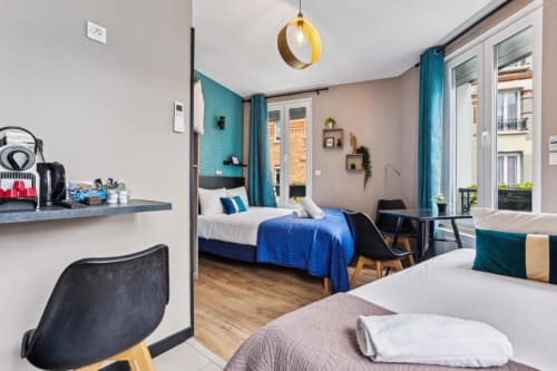 Modern studio bedroom at Résidence Aurmat Paris with twin beds, teal accents, kitchenette, and Parisian balcony views