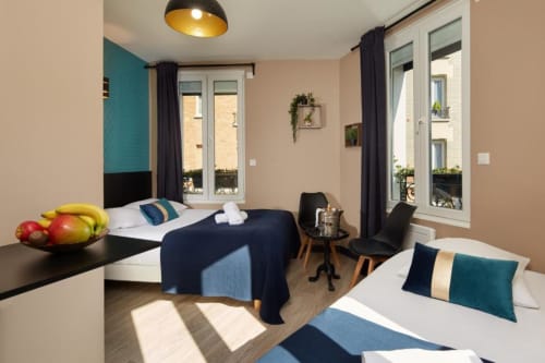 Modern studio bedroom at Résidence Aurmat Paris Boulogne with dual beds, kitchenette, turquoise accents, and balcony access