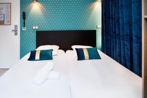 Modern twin bed studio at Résidence Aurmat Paris Boulogne with turquoise patterned walls, white linens, and dark blue