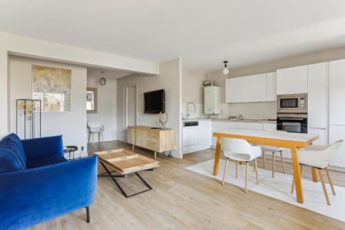 Modern 1-bedroom apartment at Résidence Aurmat Paris with open-plan living, blue sofa, dining table, and white kitchen with