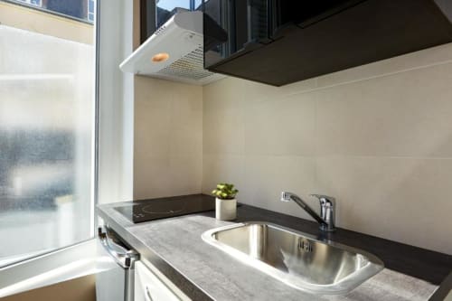 Modern kitchenette in Paris studio apartment with stainless steel sink, black countertop, and beige tile backsplash near