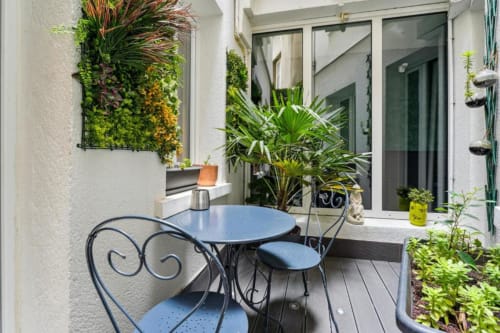 Terrasse cosy de l'hôtel Résidence Aurmat Paris avec chaises de bistrot bleues, table ronde et jardins verticaux luxuriants