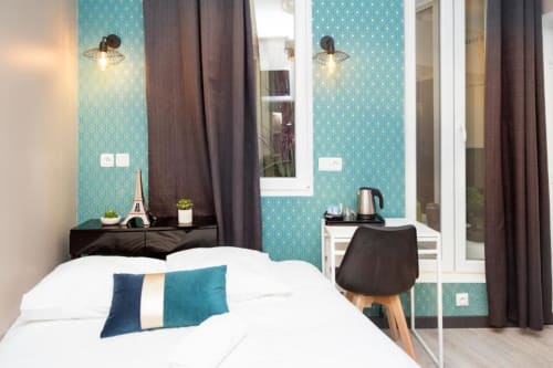 Modern hotel bedroom at Résidence Aurmat Paris with turquoise patterned walls, white bed, teal pillows, and ensuite