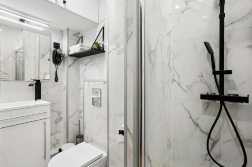 Salle de bain moderne du studio parisien avec murs en marbre, fixtures noires, douche, vasque blanche et toilettes à la Résidence Aurmat