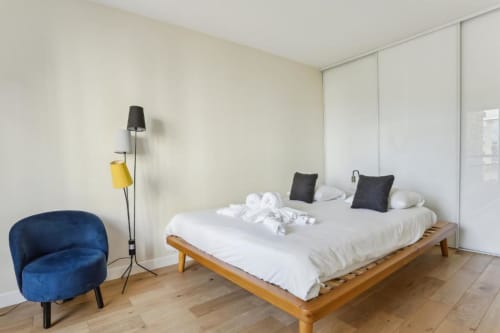 Chambre moderne à la Résidence Aurmat Paris avec lit en bois, draps blancs, fauteuil bleu et design minimaliste