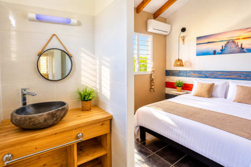 Chambre et salle de bain La cabane du pêcheur au Quetzal BnB, Sainte-Anne avec lavabo en pierre, miroir rond et style moderne