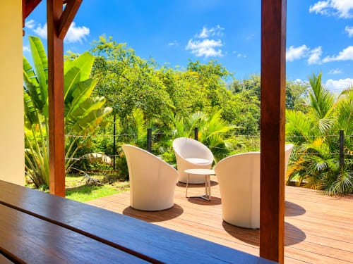 Terrasse ombragée avec chaises blanches modernes surplombant un luxuriant jardin tropical au Quetzal, Sainte-Anne